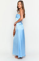 blonde model wearing a strap-back blue maxi dress with ruched lower back, gold bracelet and white hand bag