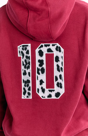 The back of a red hooded sweatshirt featuring a large number 10 applique with a black and white cow print pattern.