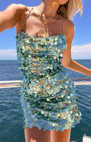 a girl poses in a aqua sequin mini dress on a boat with the ocean behind her