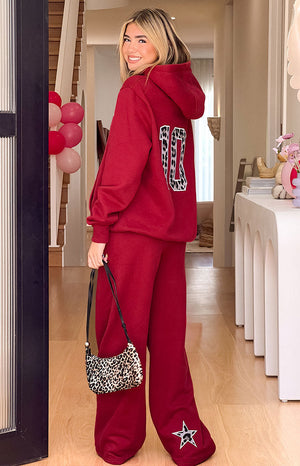 A pair of red wide-leg sweatpants featuring a large white star applique with a cow print pattern near the hem of the pant leg.