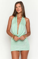 a green sparkly mini dress is worn by a blonde model standing on a boat