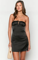 Girl wearing black strapless mini dress holding cocktail glass in front of bar area.