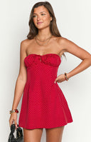 Fashion model showcasing a playful red and white polka dot strapless mini dress with a ruffled neckline and charming front tie- perfect for a casual or festive occasion.