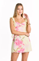 A light yellow floral mini-dress with a pink and fuchsia print featuring a bow detail at the bust and ruffled shoulder straps. Our dress is suitable for a semi-formal summer event or a party.
