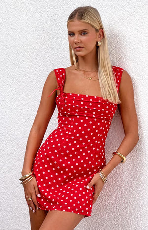 Blonde model wearing a red polka dot mini dress with ribbons at the straps and gathered bust details