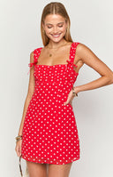Blonde model wearing a red polka dot mini dress with ribbons at the straps and gathered bust details
