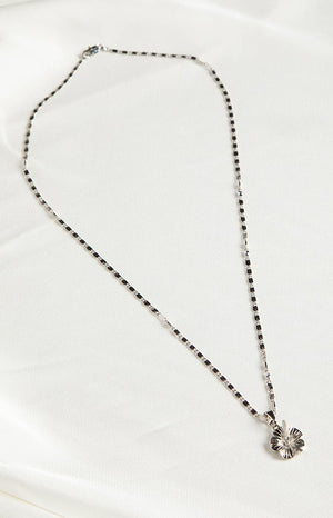 Brunette girl wearing a silver flower necklace and white top.