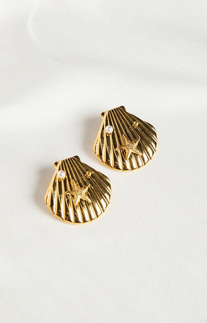Brunette girl wearing gold seashell earrings with a starfish and pearl.