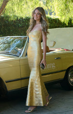 Side view of a gold strapless bandage maxi dress with a fitted bodice and flared mermaid hem