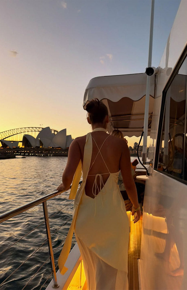 Rear view of a yellow satin maxi dress with a low scoop back, criss-cross tie straps, and a long scarf detail