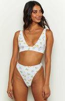 Close-up of the V-neckline and wide underbust band of a white floral bikini top with yellow and purple flowers