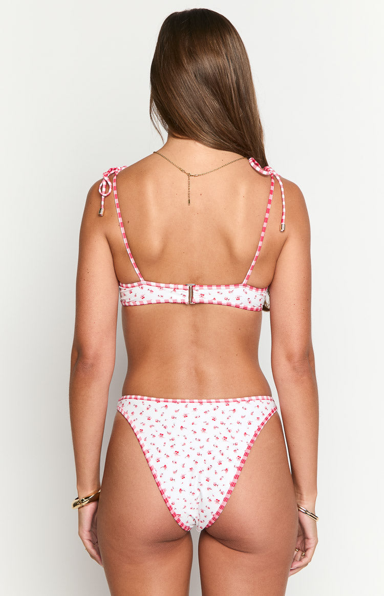 Rear view of a white bikini top with red floral print, red gingham tie shoulder straps, and gold back clasp