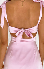 Rear view of a pink satin mini dress showing the large tie-back detail, waist cutouts, and shoulder ties