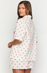 Side view of a white short-sleeve collared shirt with red cherry print, embroidered B, and matching pajama shorts
