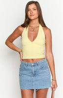 Model sitting down and is wearing a yellow halter top and white ruffle shorts. She is also wearing a shell necklace.