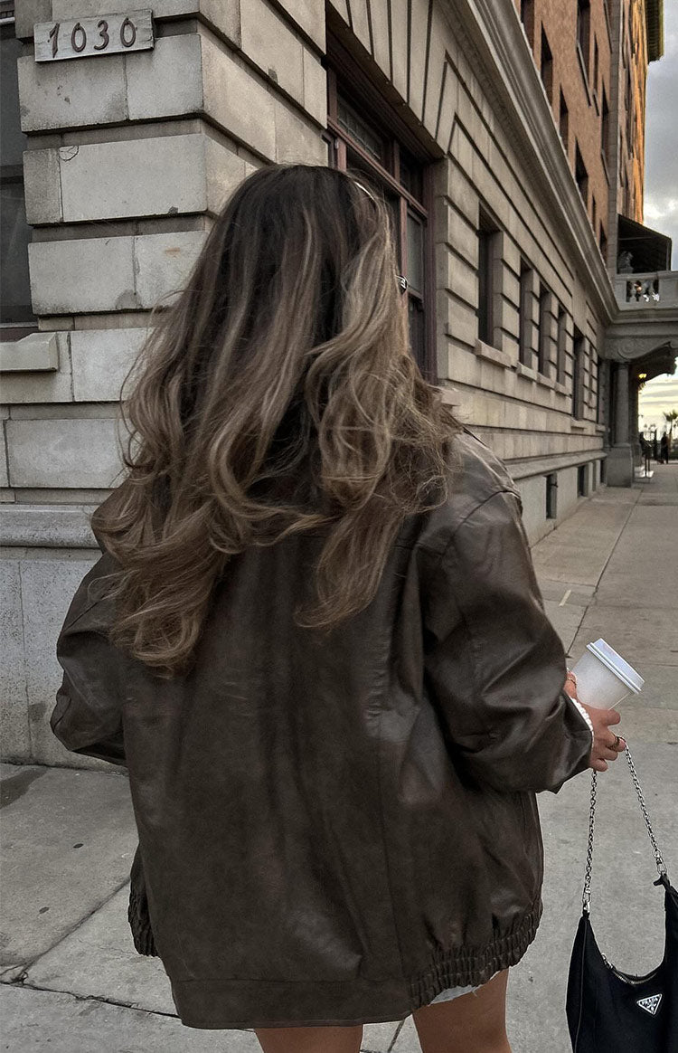 Faux leather oversized brown bomber jacket. Worn by model walking the street. 