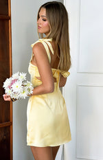 Side view of a yellow satin mini dress with tie shoulders, side cutouts, and a tie-back detail