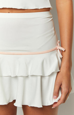 Detail shot of the pink velvet bow and trim accenting the side of a white tiered mini skirt