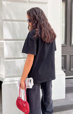 Rear view of a black oversized tee with short, loose sleeves and a relaxed, straight hem