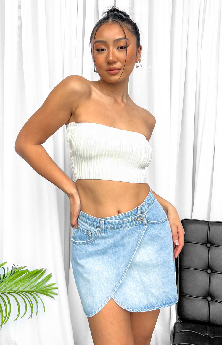 Light wash denim mini skirt with an asymmetrical wrap front and a single button closure at the waist