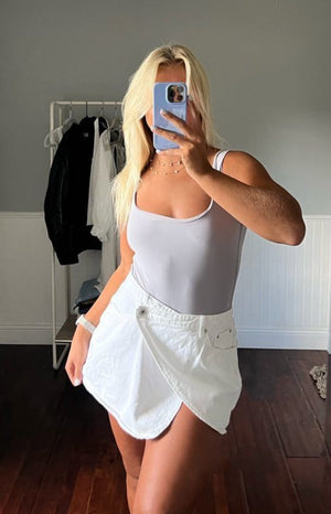 Front view of a white denim asymmetrical wrap mini skirt with a single button closure and front pockets