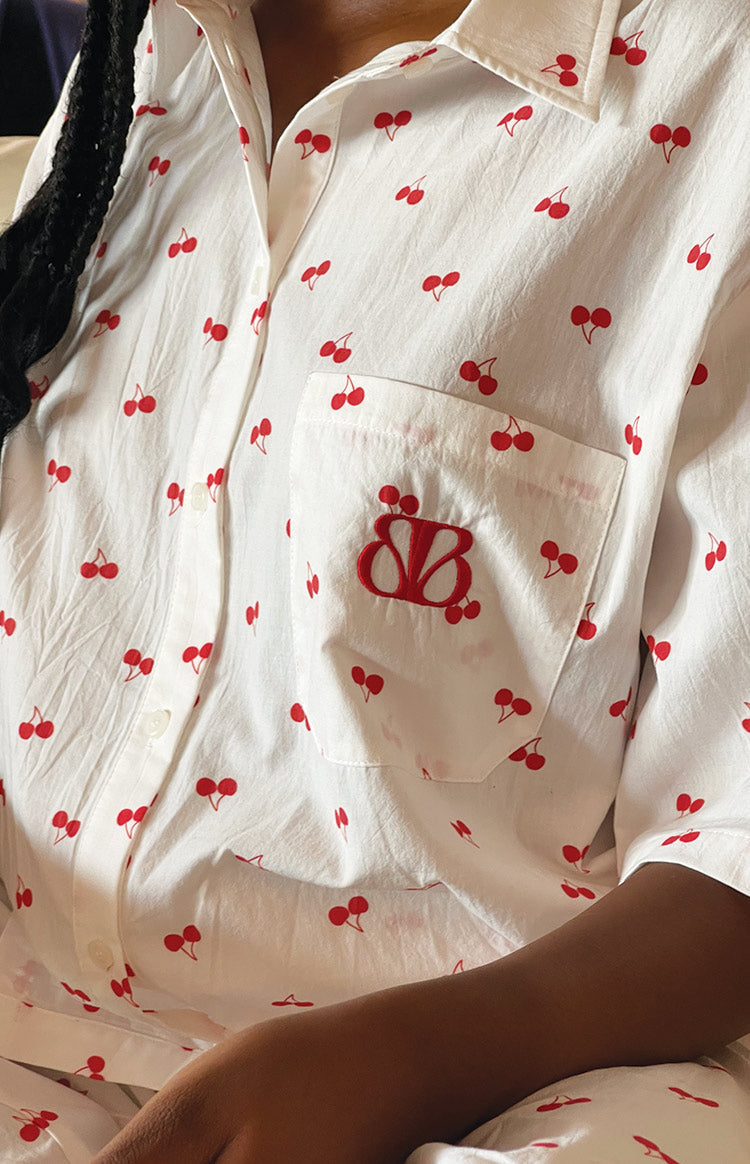 Close-up of the red embroidered logo on the chest pocket of a white cherry print pajama shirt