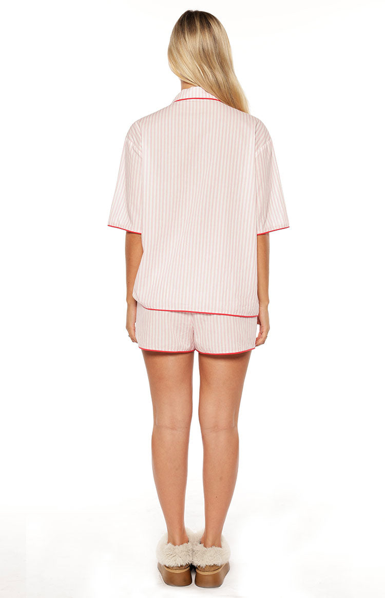 Rear view of a pink striped pajama shirt with short sleeves and matching shorts, both with red piping