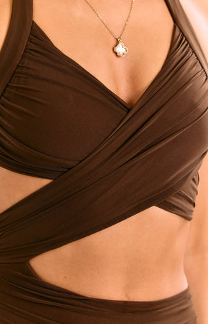 Model wears a chocolate brown maxi dress with a halter neckline. This formal dress features a daring waist cut out and a fitted silhouette. A perfect choice for a wedding guest or special event outfit.
