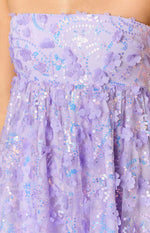 Close-up of the purple mini dress showing 3D floral appliques and a swirling pattern of iridescent sequins