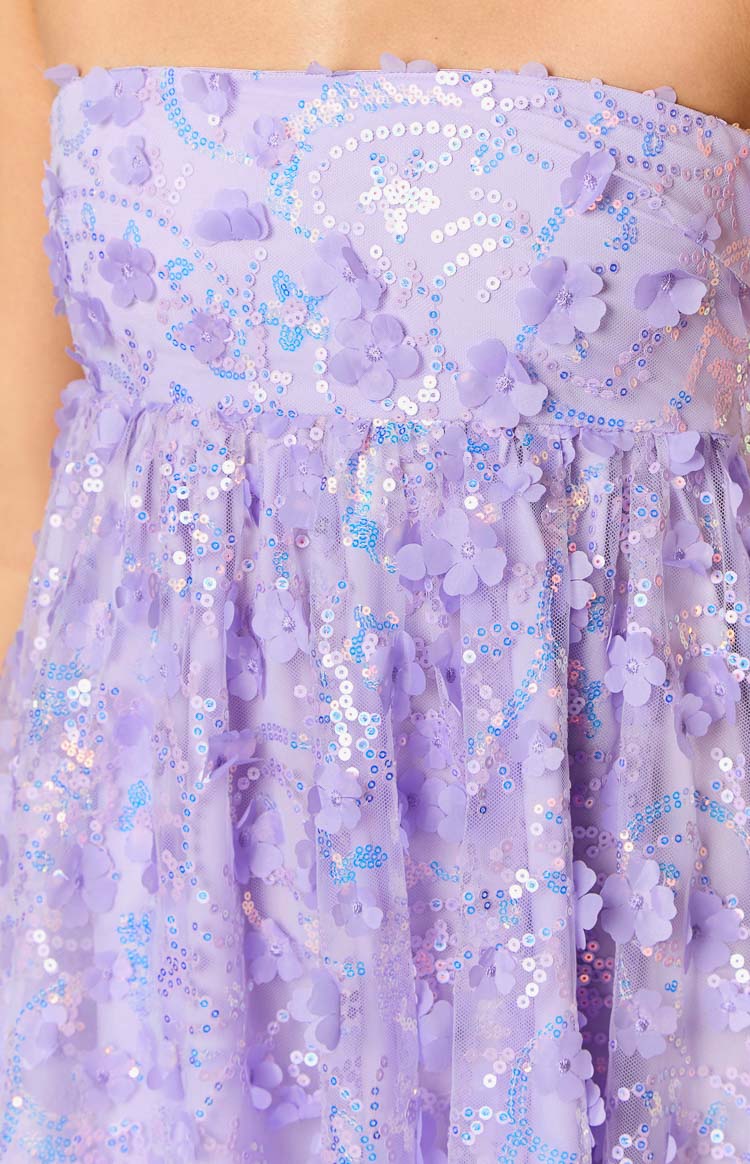 Close-up of the purple mini dress showing 3D floral appliques and a swirling pattern of iridescent sequins