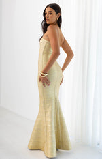 Side view of a gold strapless bandage maxi dress with a fitted bodice and a mermaid-style flared hem