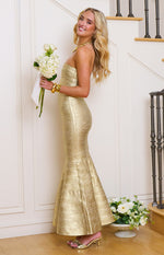 Side view of a gold bandage strapless maxi dress showing the fitted silhouette and flared mermaid hem