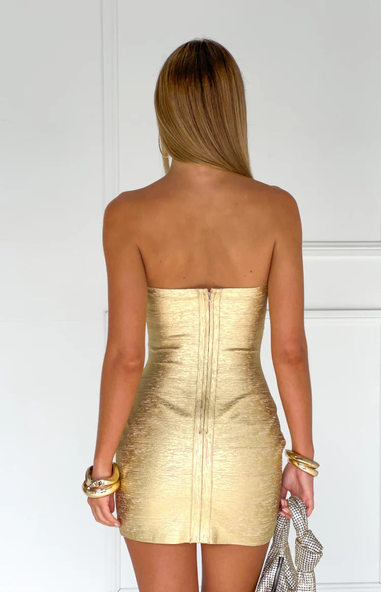 Rear view of a gold bandage strapless mini dress with an exposed zipper down the back