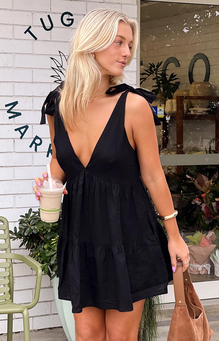 A tiered black mini dress with a plunging V-neckline and charming tie-shoulder straps- offering a sweet and casual style.