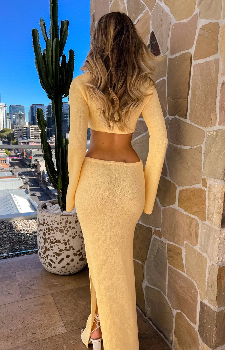 Rear view of a yellow textured knit maxi dress with an open back, cropped top, long flared sleeves, and a side slit