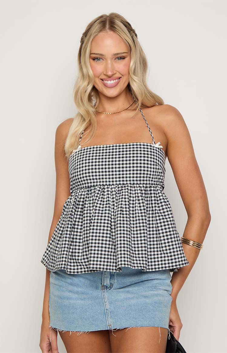 Front view of a black and white gingham halter top with a straight neckline, small bow details, gathered waist, and peplum hem