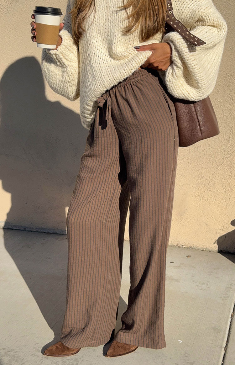Side view of brown pants with thin vertical stripes, showing the drawstring waist and relaxed wide-leg fit