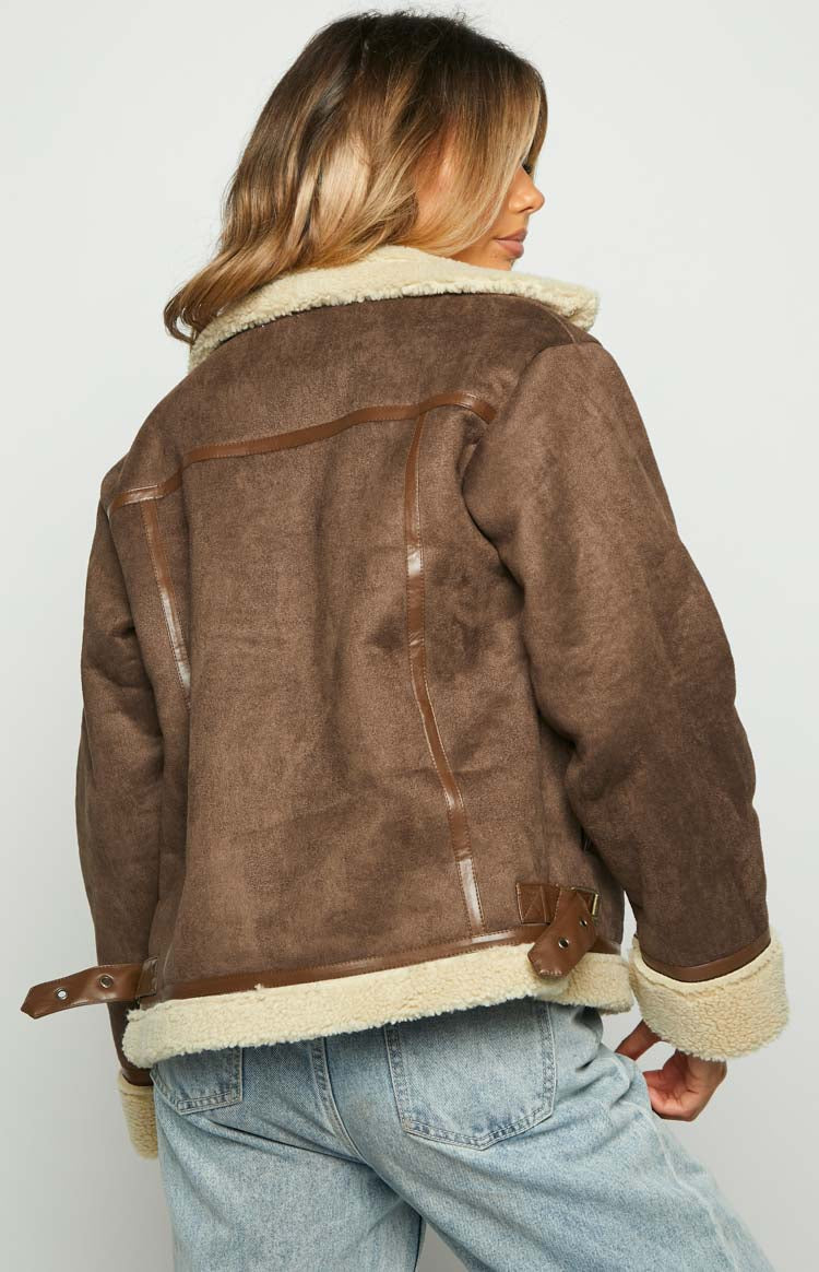 Rear view of a brown sherpa jacket with cream lining, brown faux leather piping, and buckle straps at the hem