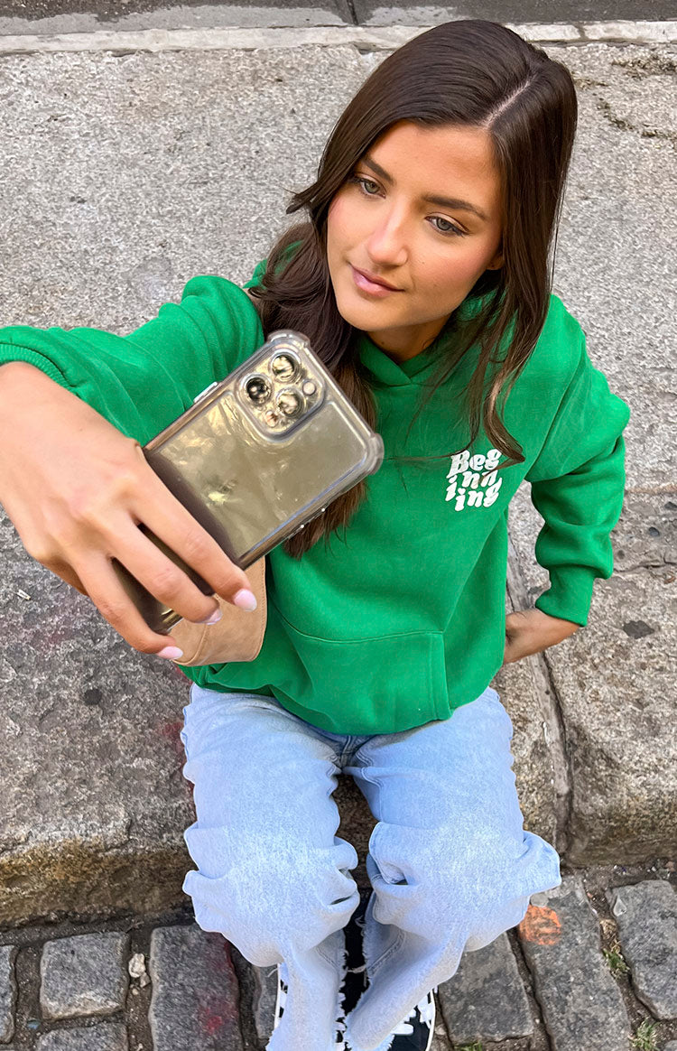 Close-up of the white 'Beginning' text logo on the chest of a green oversized hoodie with a kangaroo pocket