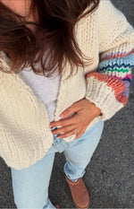 Top-down view of a cream chunky knit cardigan with wide sleeves featuring multi-coloured stripes