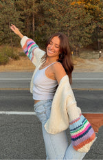 Side view of a cream chunky knit cardigan with wide bell sleeves and colourful horizontal stripes