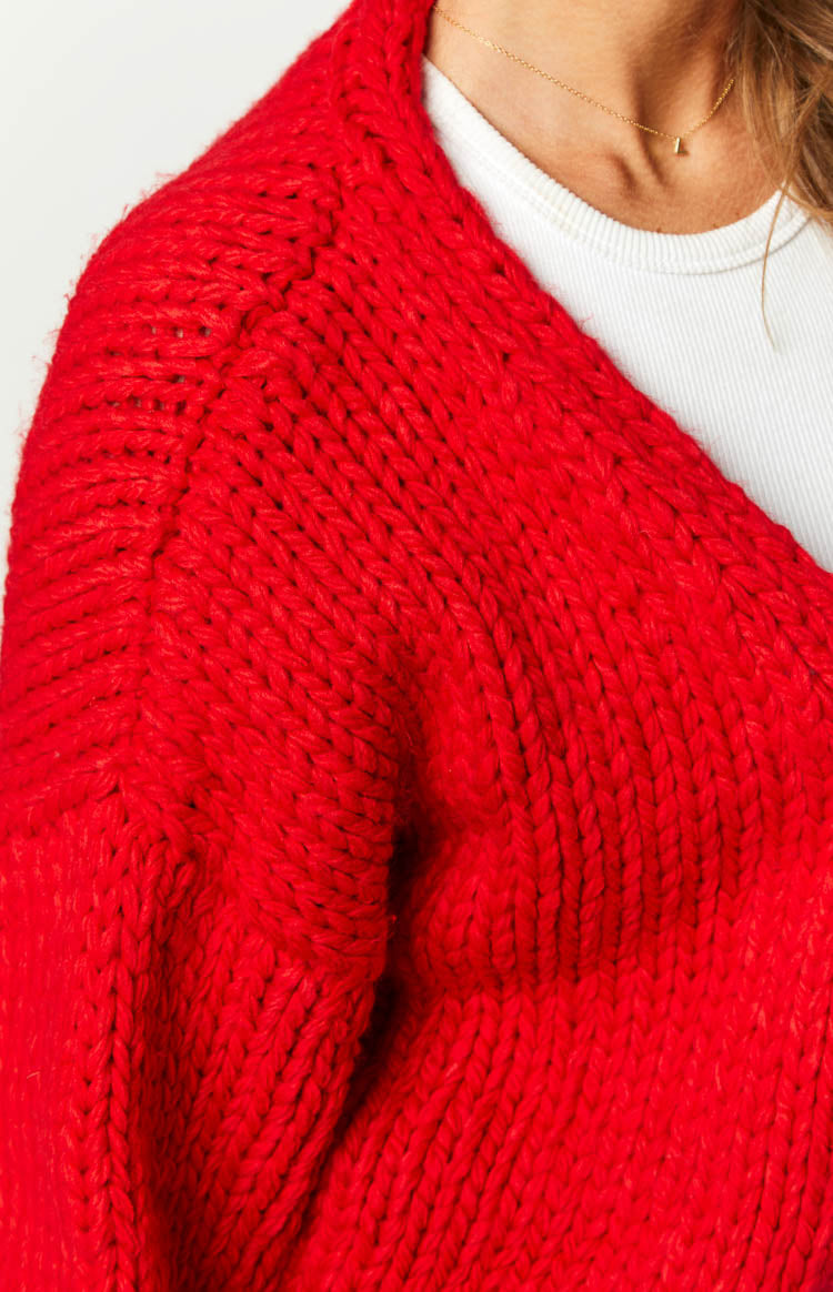 Close-up of the chunky red knit texture on the shoulder and upper arm of the cardigan