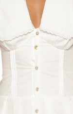 Detail shot of the white mini dress bodice with scalloped lace collar, pearlescent buttons, and pintuck panels