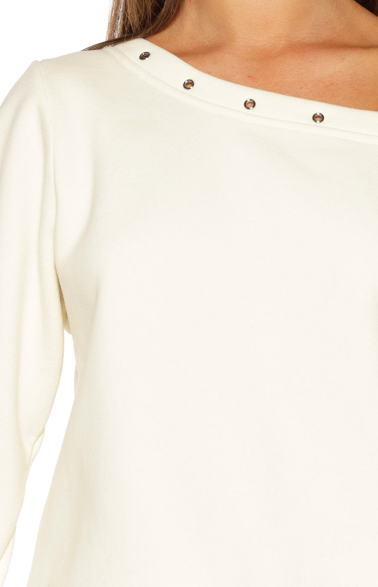Close-up of the cream sweater's asymmetric neckline with a row of silver eyelets