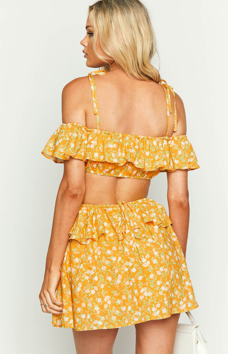 Rear view of an orange floral mini dress with tie-up shoulder straps, off-shoulder ruffle, and back waist tie detail