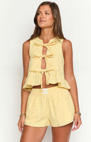 a girl with blonde hair wears a yellow and white gingham top with bows and a matching pair of boxer shorts and a gold bracelet