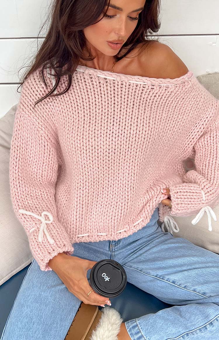 Close-up of the baby pink chunky knit sweater with white tie details on the shoulder and ribbed cuff