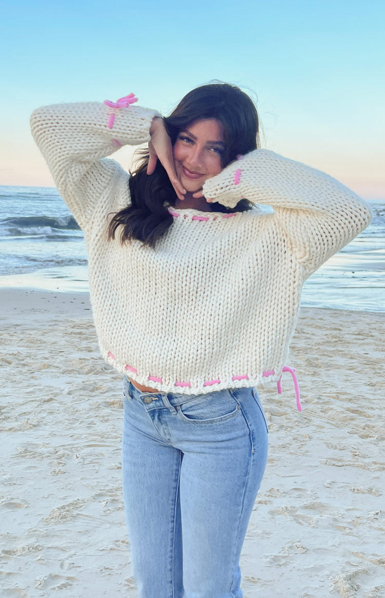 Cream chunky knit sweater with pink ribbon stitching along the boat neck, cuffs, and hem