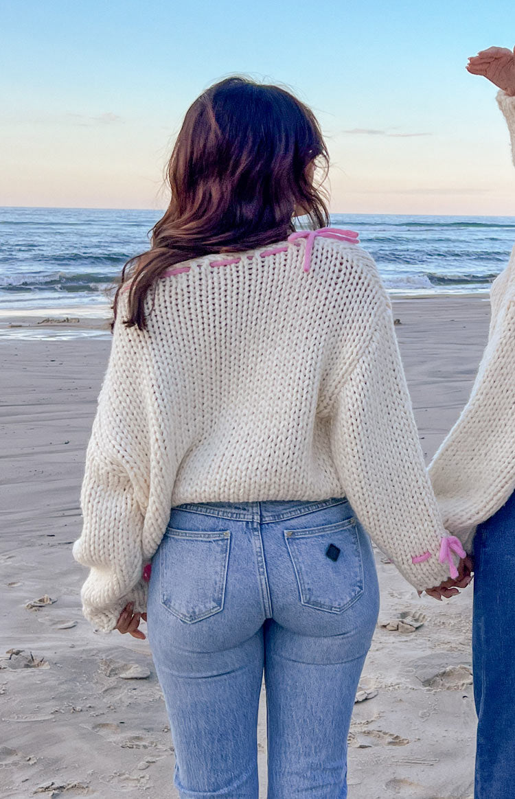 Rear view of a cream chunky knit sweater with pink tie details on the shoulders and cuffs