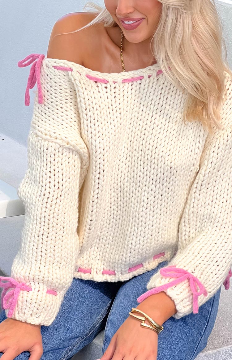 Close-up of a cream chunky knit off-shoulder sweater with pink tie details on the shoulders and cuffs